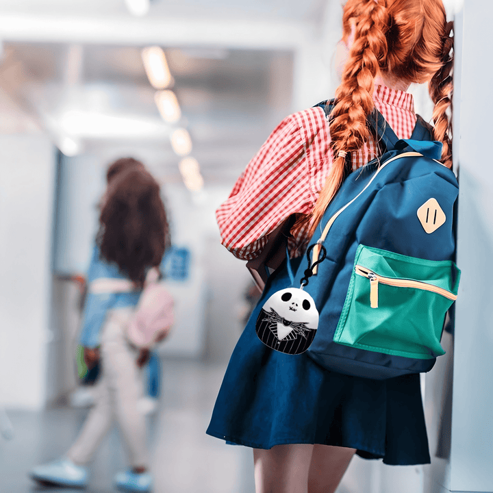 Girl with red braids carries a green and blue backpack featuring a Jack Skellington Squishmallow clip.