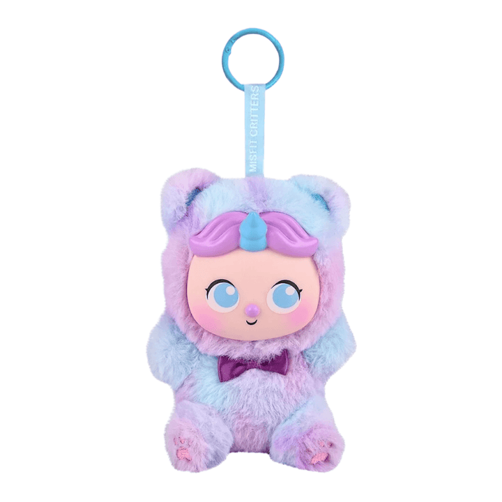 A plush character keychain or bag charm with a fuzzy pastel body in lavender, pink, and light blue, featuring a large cartoon face, blue key ring, and a hanging tag that reads 'MOSTLY LIGHTS'.