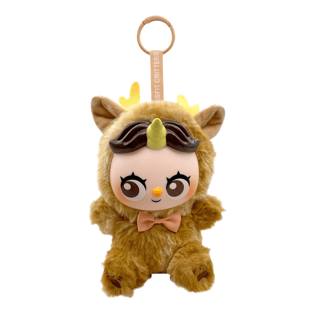 A plush character keychain or bag charm shaped like a cute cartoon creature in a brown deer-like outfit, with a peach face, large eyes, a pink bow tie, and a light wood ring at the top. The fabric reads 'BEST CRAFTERS' vertically on the strap.