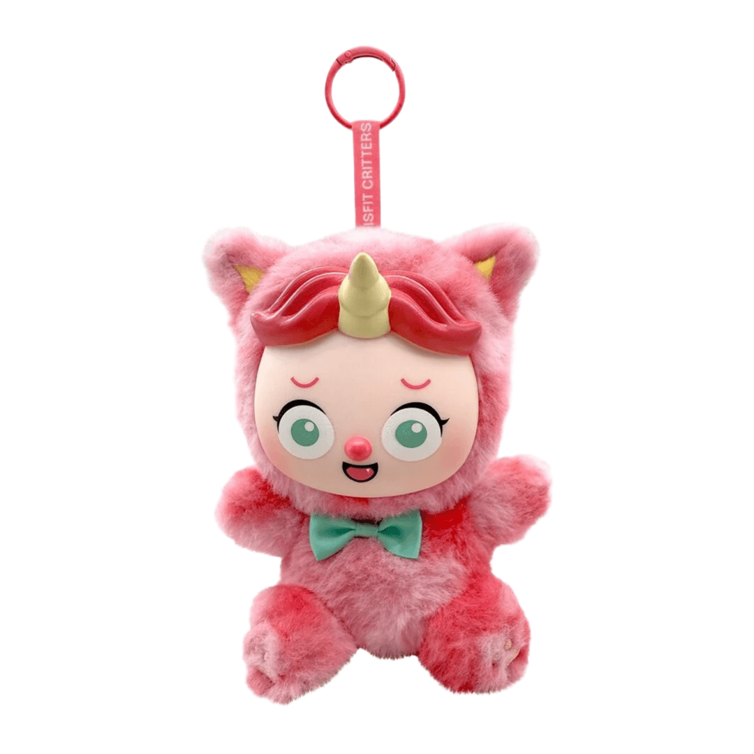 A pink plush character keychain or bag charm with a unicorn horn, large green eyes, and a mint green bow tie, hanging from a pink ring strap labeled 'SOFT CHITTERS' on a plain white background.
