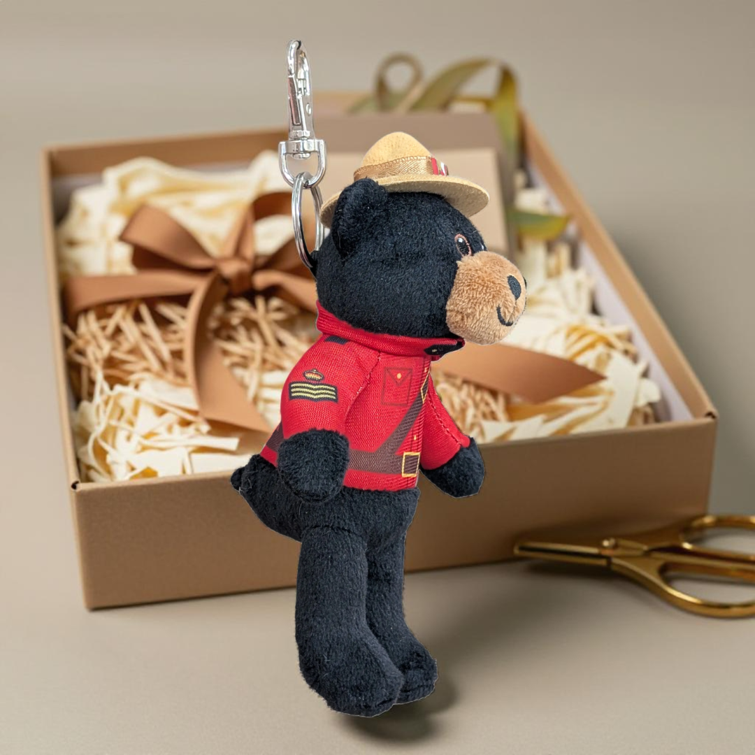 RCMP Black Bear Animal Keychain wearing a red Mountie-style uniform and tan hat, displayed in front of a gift box
