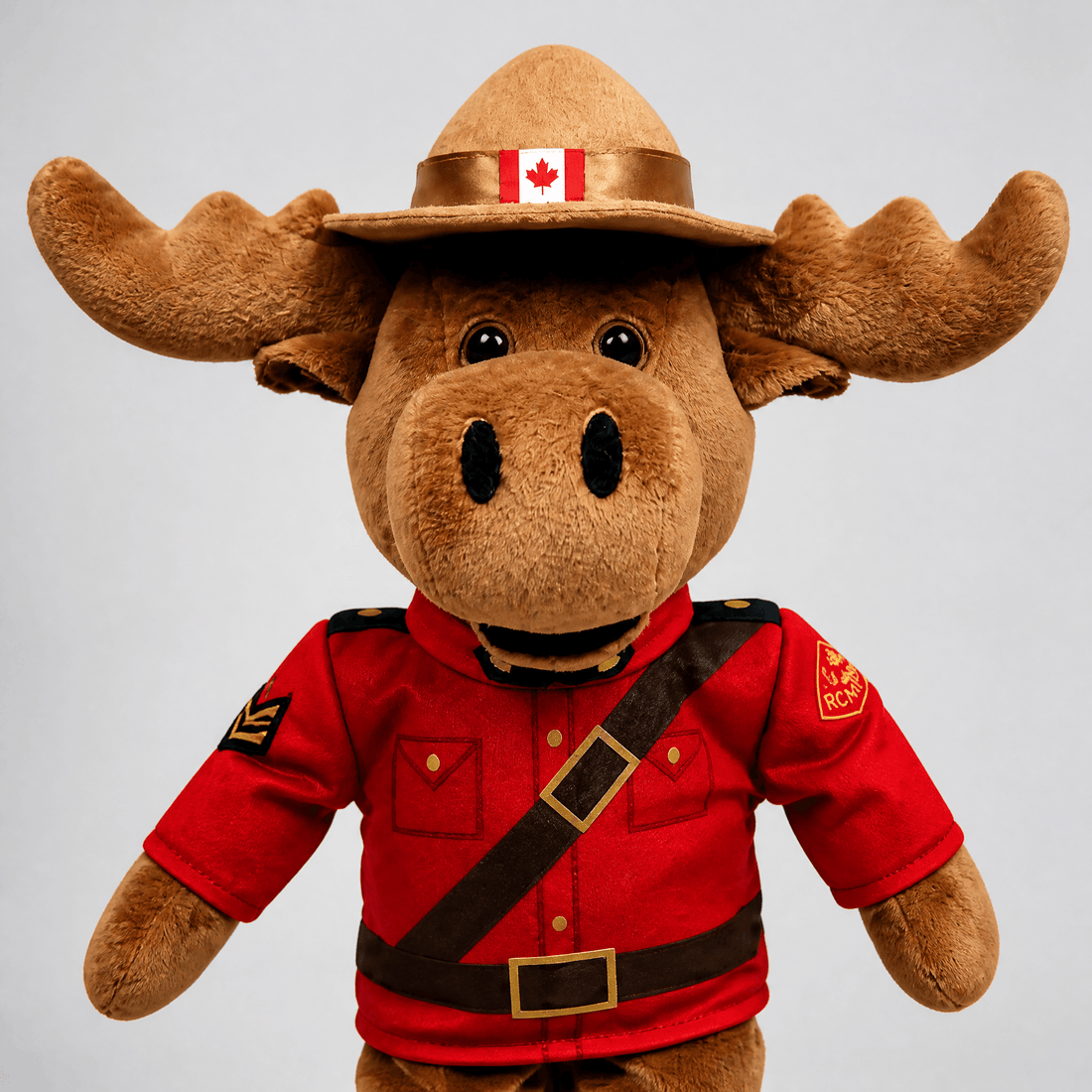 Plush moose toy wearing a red uniform and Canadian hat with flag on a gray background