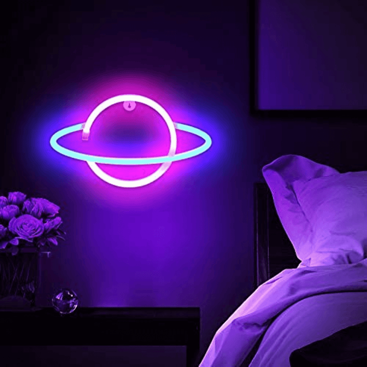 Saturn Neon Wall Light - Led Sign illuminating a bedroom with pink and blue glow.