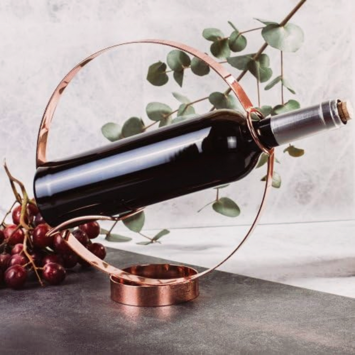 Elegant wine bottle holder and pourer showcasing a curved copper frame with a wine bottle and grapes.