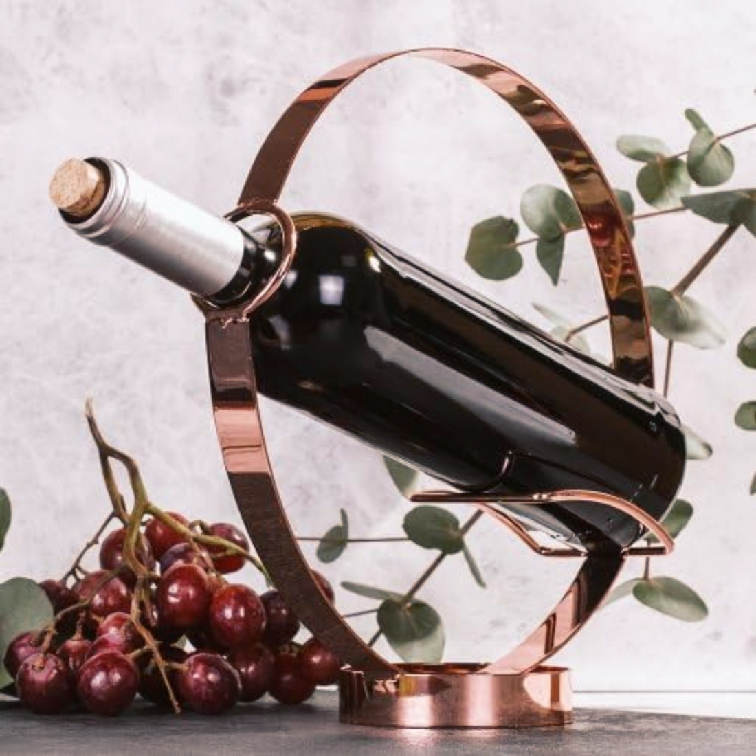 Elegant wine bottle holder and pourer showcasing a wine bottle in a stylish metallic stand with grapes in the background.