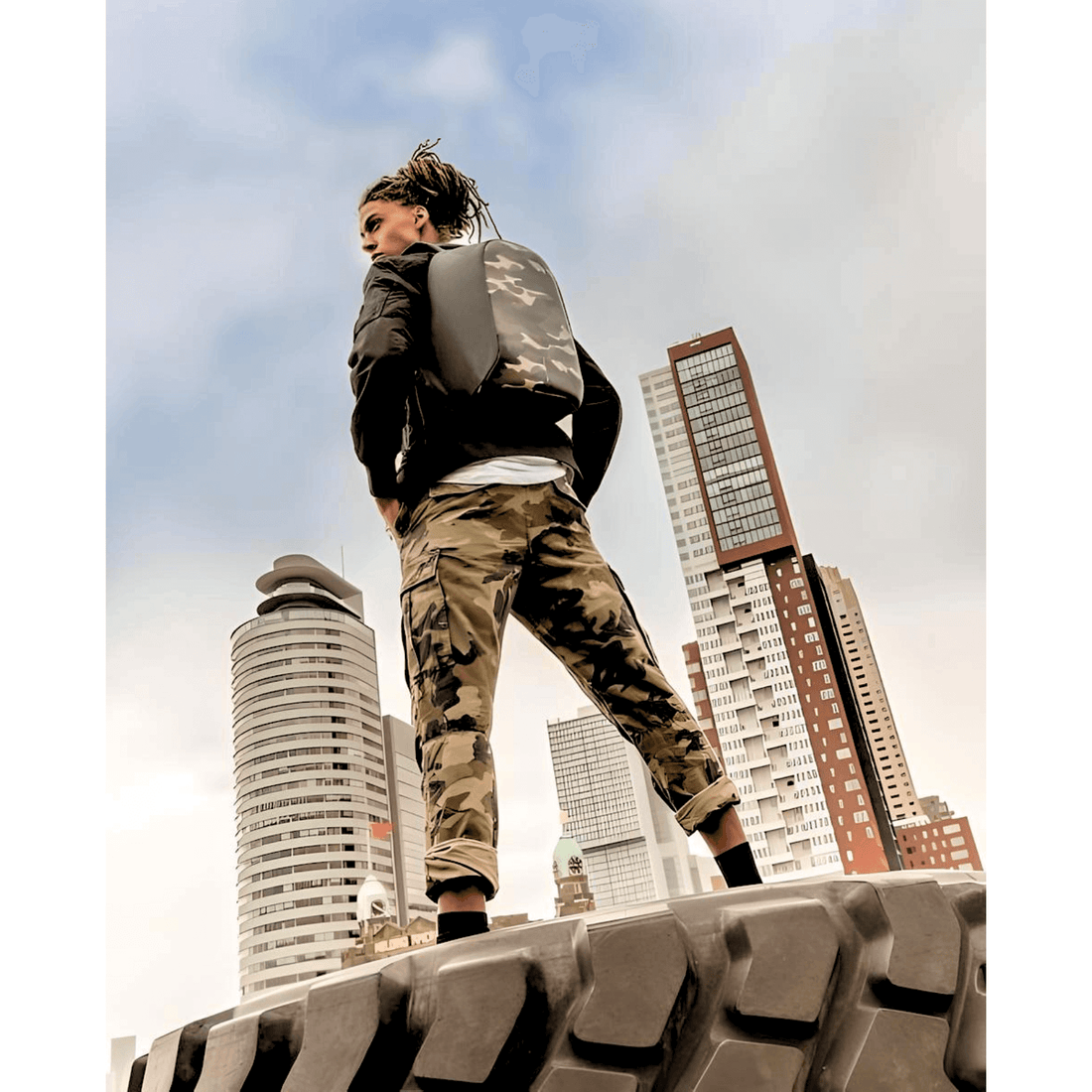 Model showcasing XD Design Bobby Compact Anti-Theft Backpack in Camouflage Green against a city skyline.