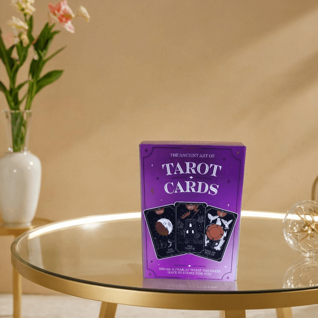 Ancient Art of Tarot Cards 78-card deck displayed on a stylish table with flowers in the background.