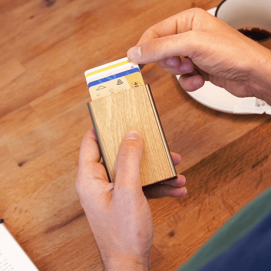 Person holding an OGON Slider Automatic Card Holder in Bamboo, part of the anti-theft backpack and RFID card holder set.