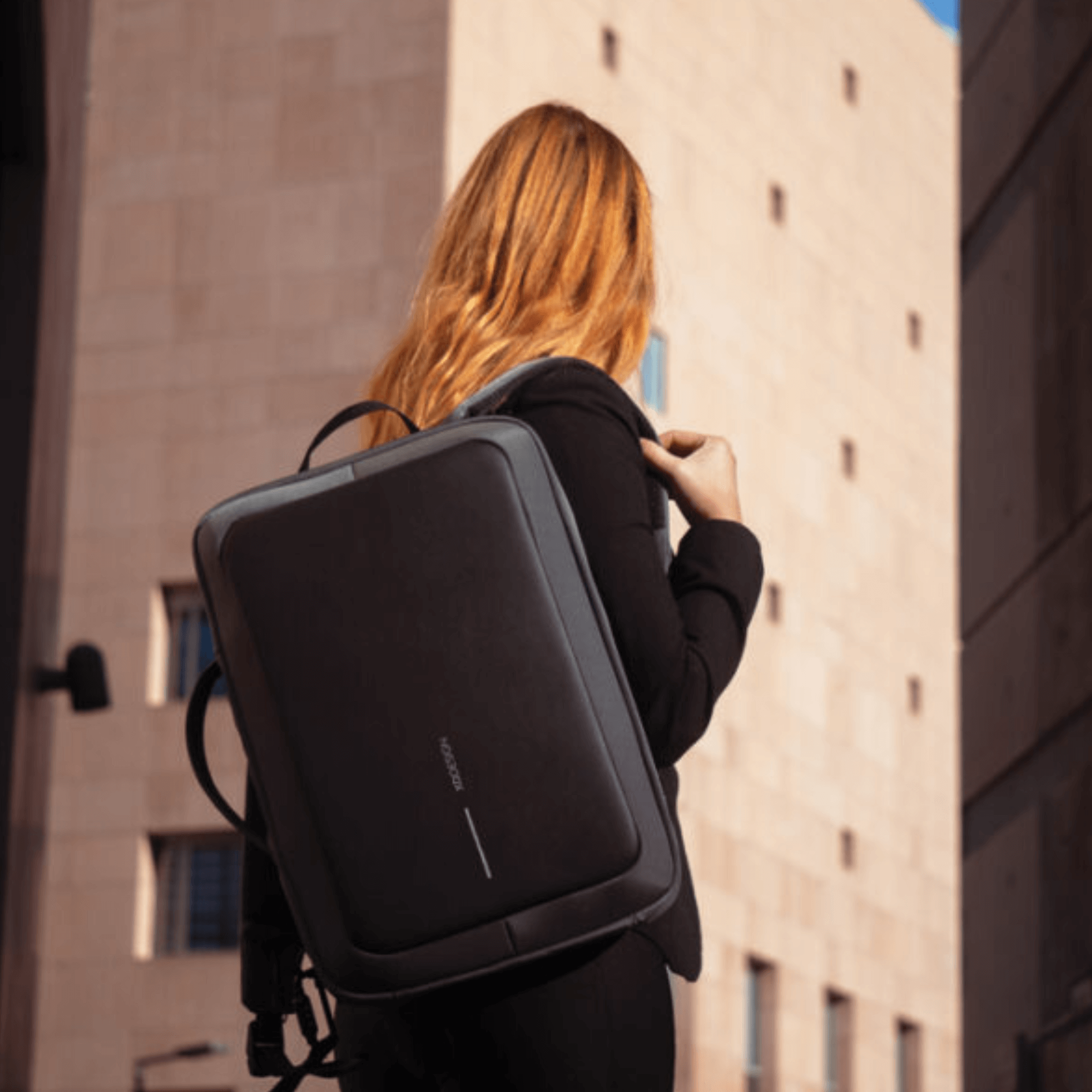 Woman wearing Bobby Bizz 2.0 anti-theft backpack in black, stylishly walking in an urban setting.