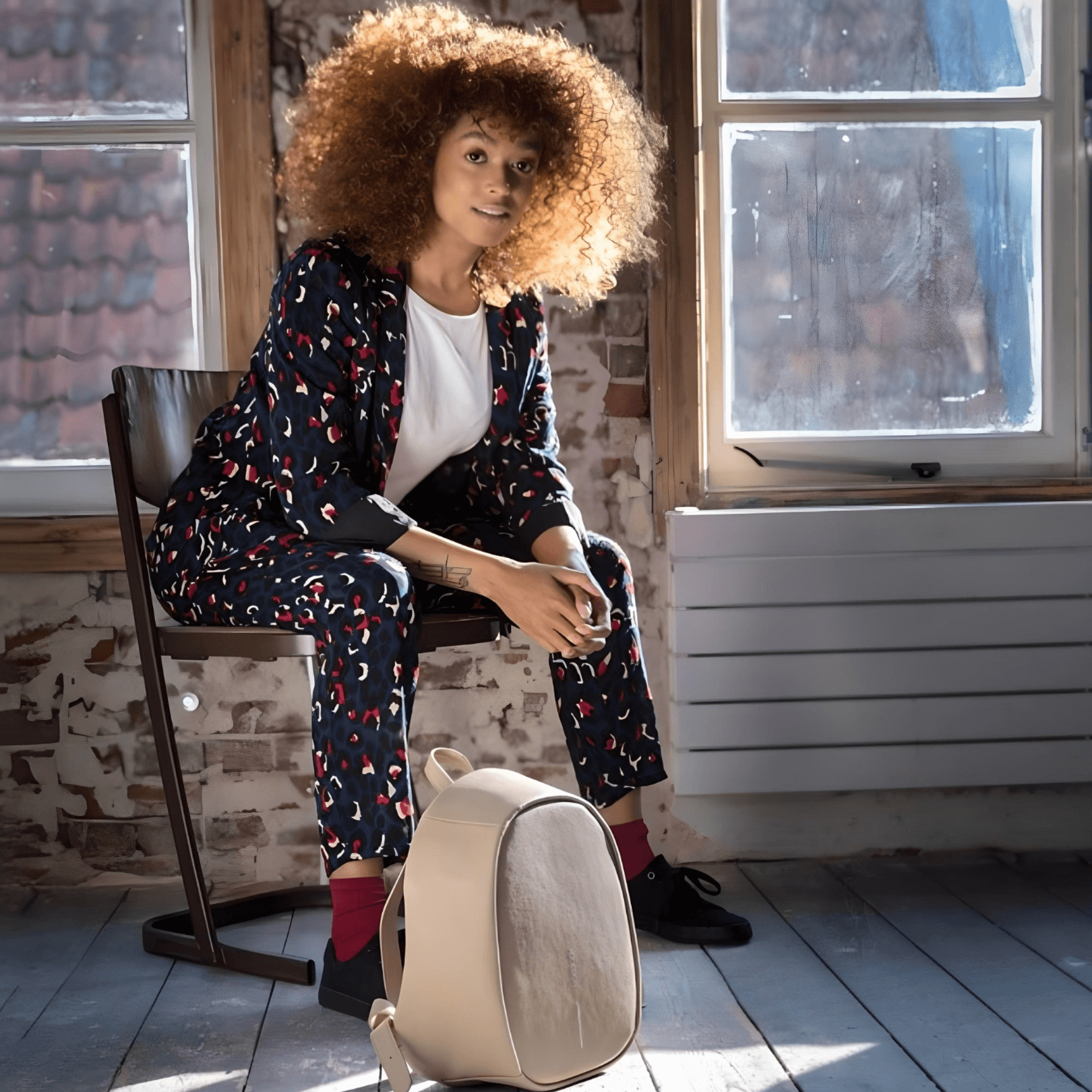Bobby Elle Anti-Theft Backpack Brown next to a person sitting in a stylish indoor setting.