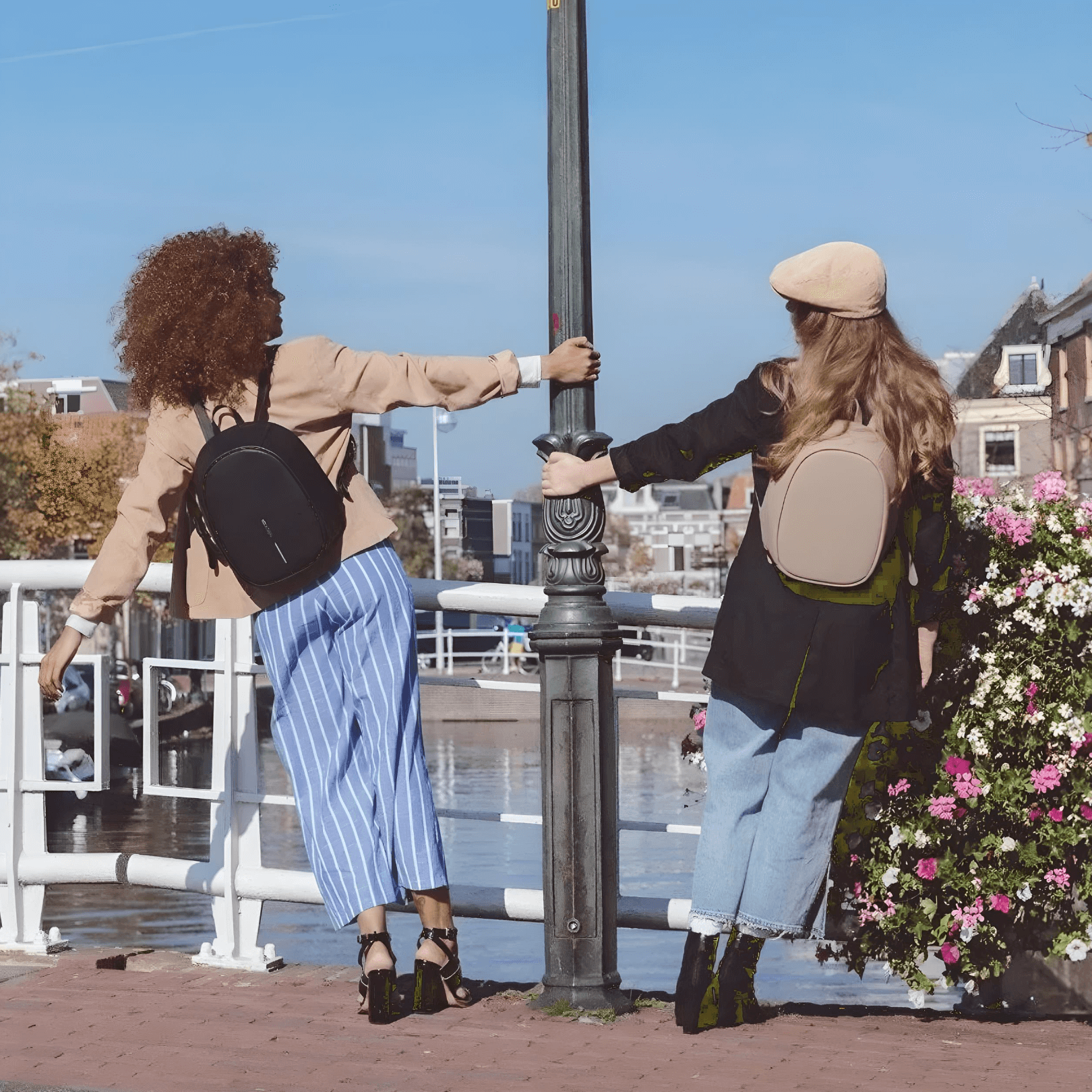 Two models wearing Bobby Elle Anti-Theft Backpack Brown by a canal, showcasing style and security in fashion.