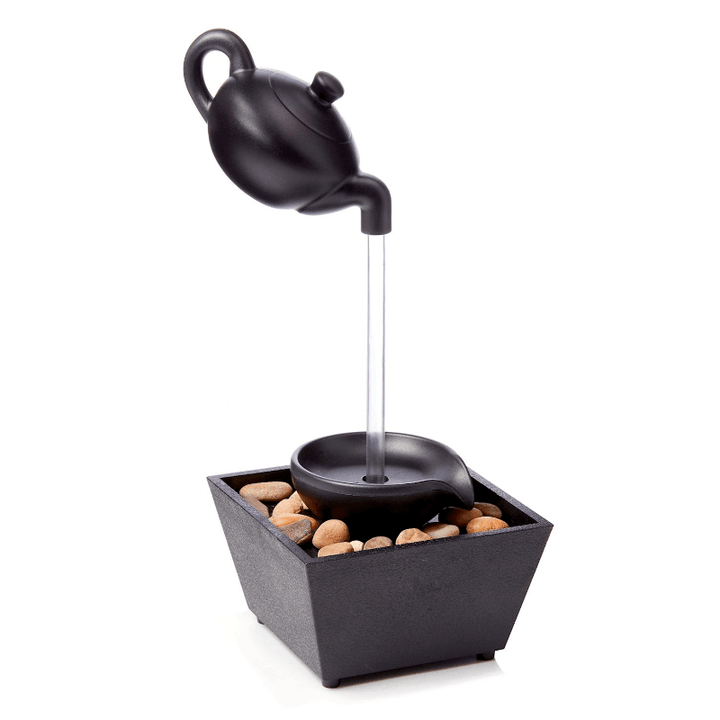 Floating teapot table fountain with LED light and pebbles, creating a serene indoor water feature.