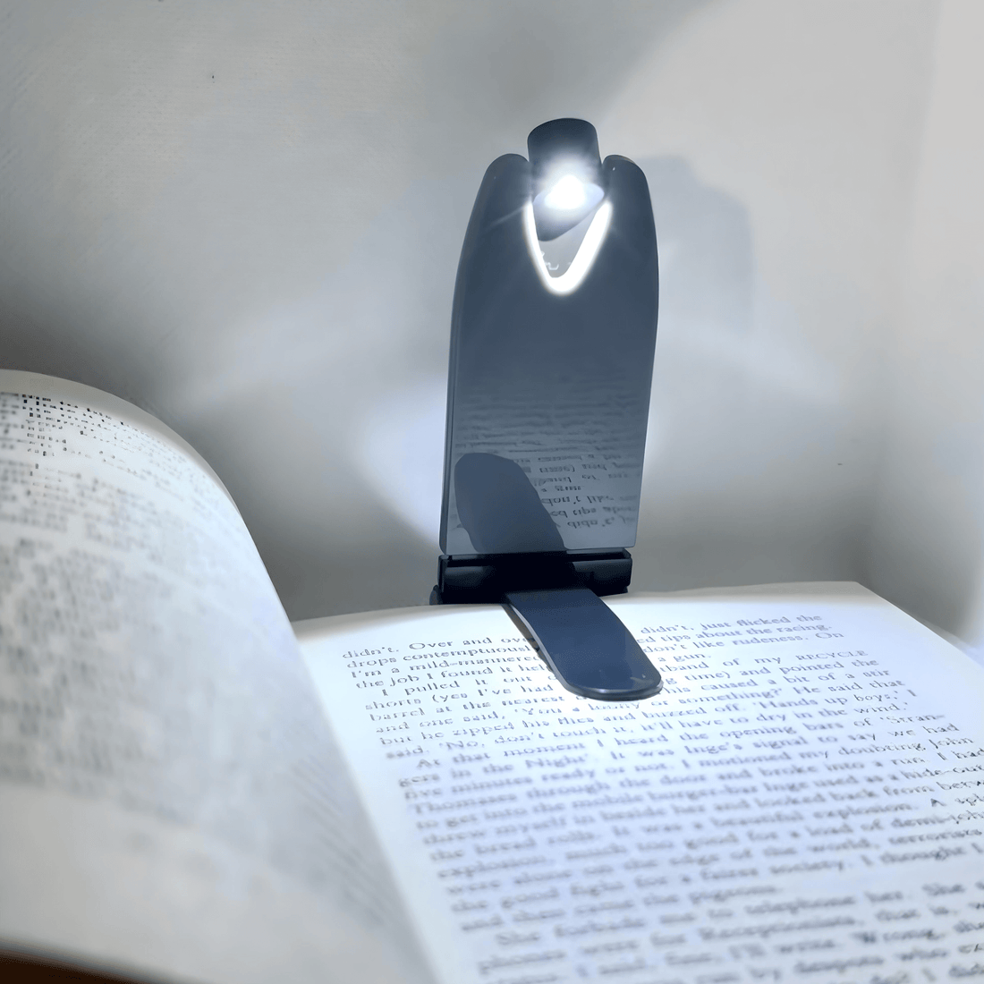 Foldable LED book light illuminating open pages of a book, showcasing its compact and sleek design.