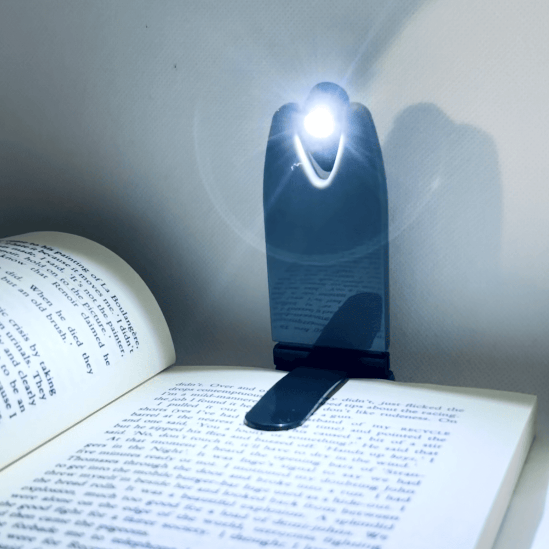 Compact foldable LED book light illuminating an open book for convenient reading.