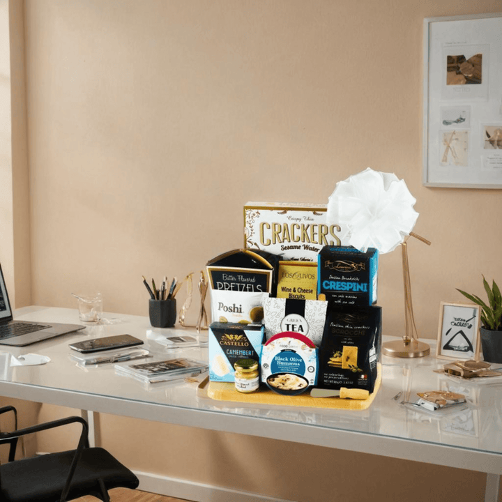 Gourmet snack gift basket featuring crackers, pretzels, tea, and more on a modern desk setting.