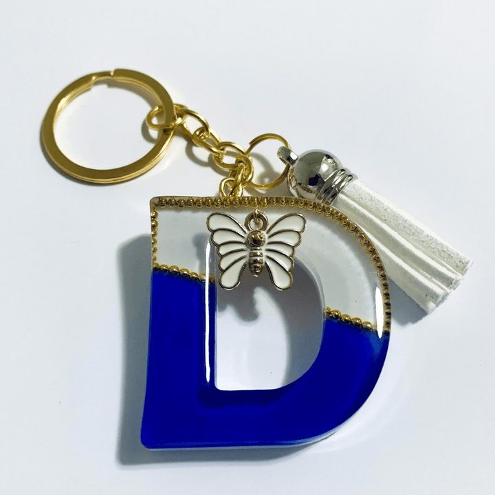 Keychain - Letter D featuring a handcrafted marbled design in white and blue with decorative butterfly and tassel.