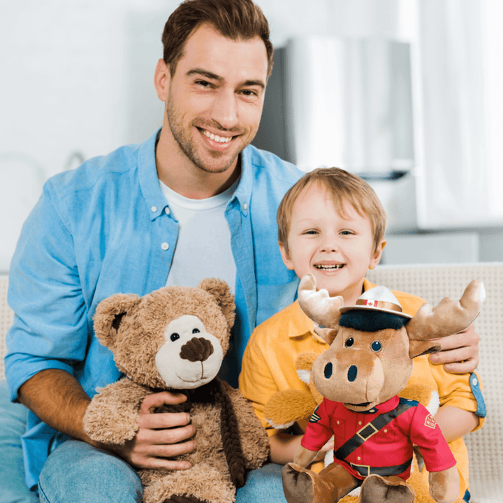 A father and son hold plush toys, including a RCMP Sergeant Moose, celebrating Canadian heritage.