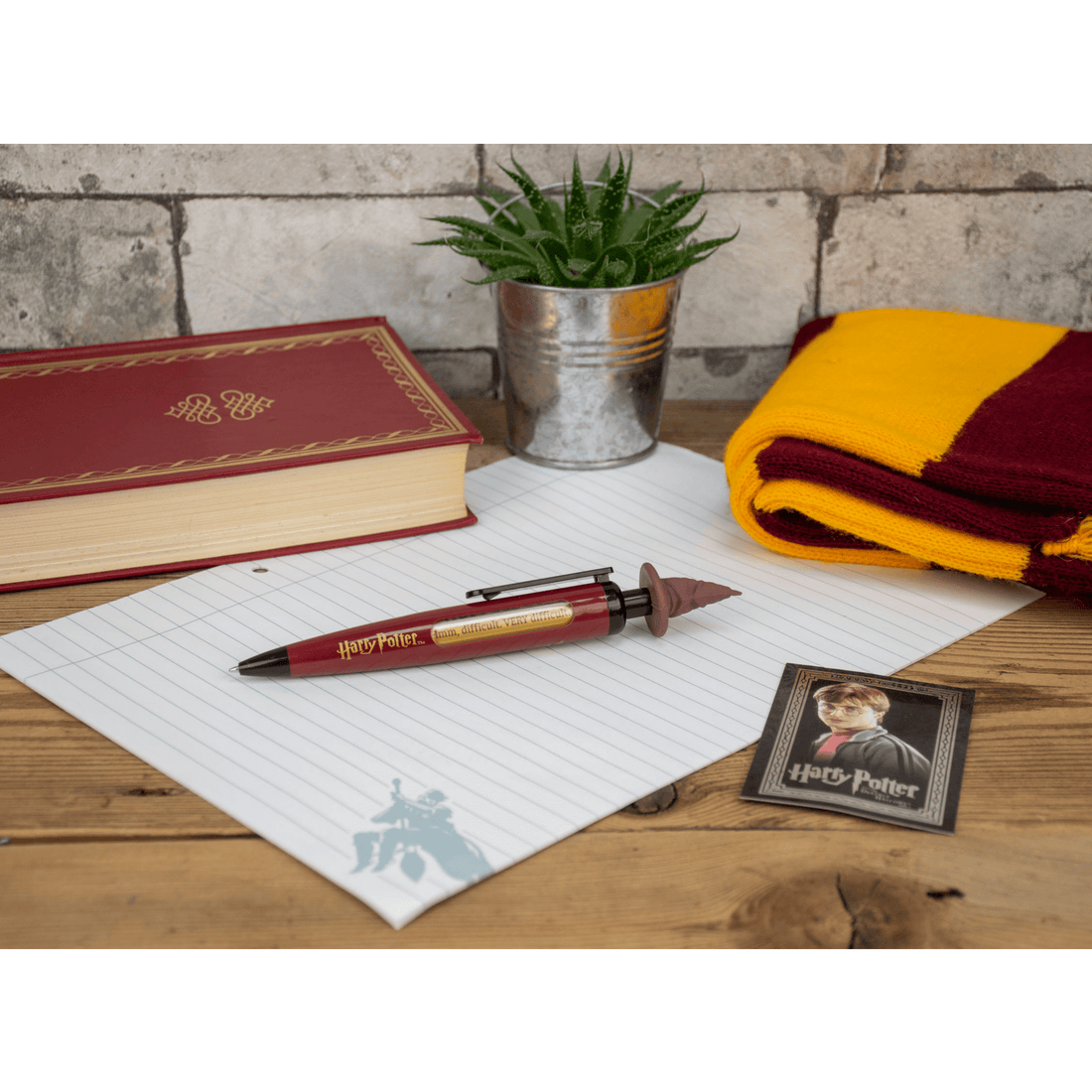 Harry Potter Sorting Hat pen on a desk with Hogwarts book, notepad, and Gryffindor scarf.