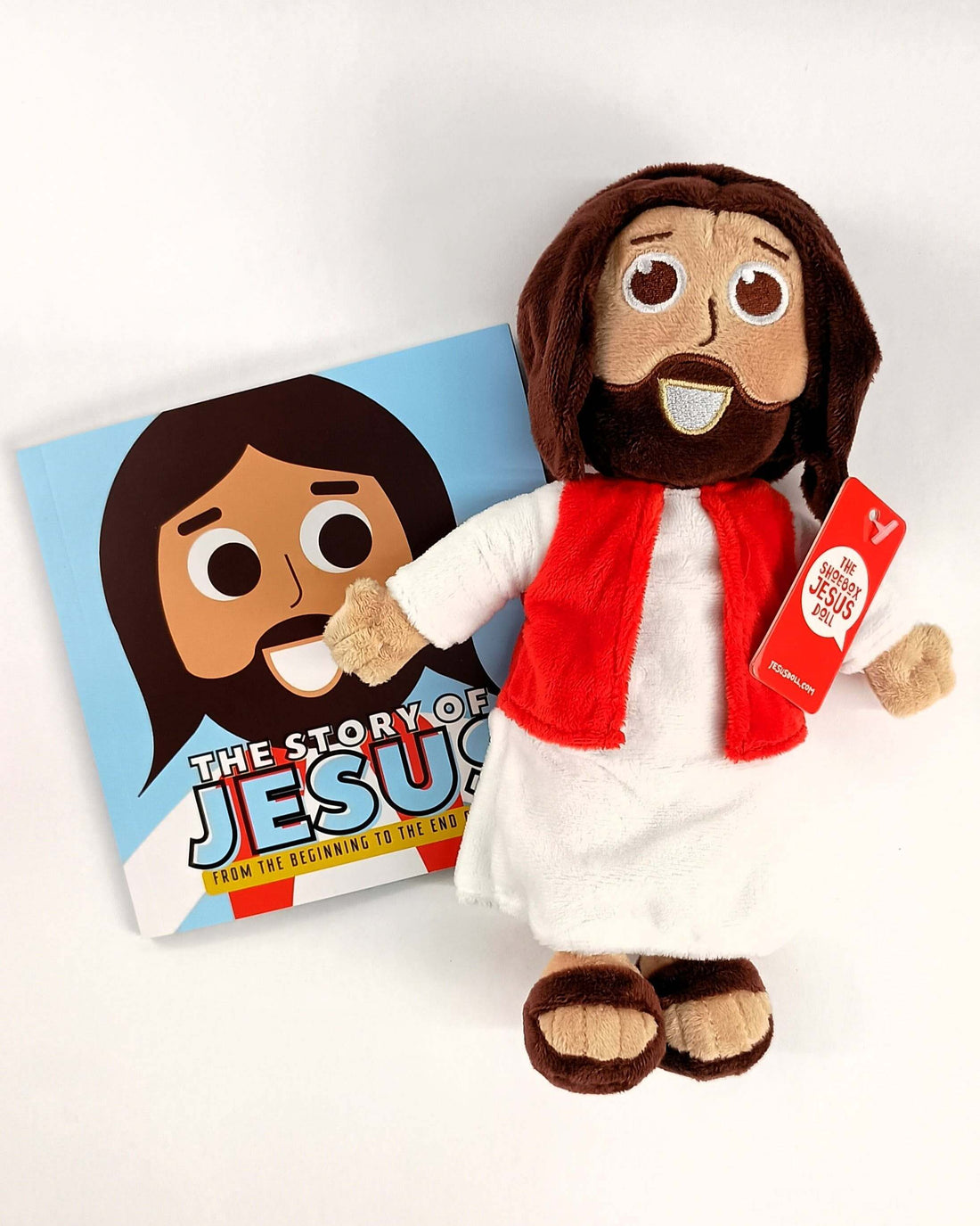 Plush Jesus doll with a red scarf next to a children's book titled 'The Story of Jesus' for kids.