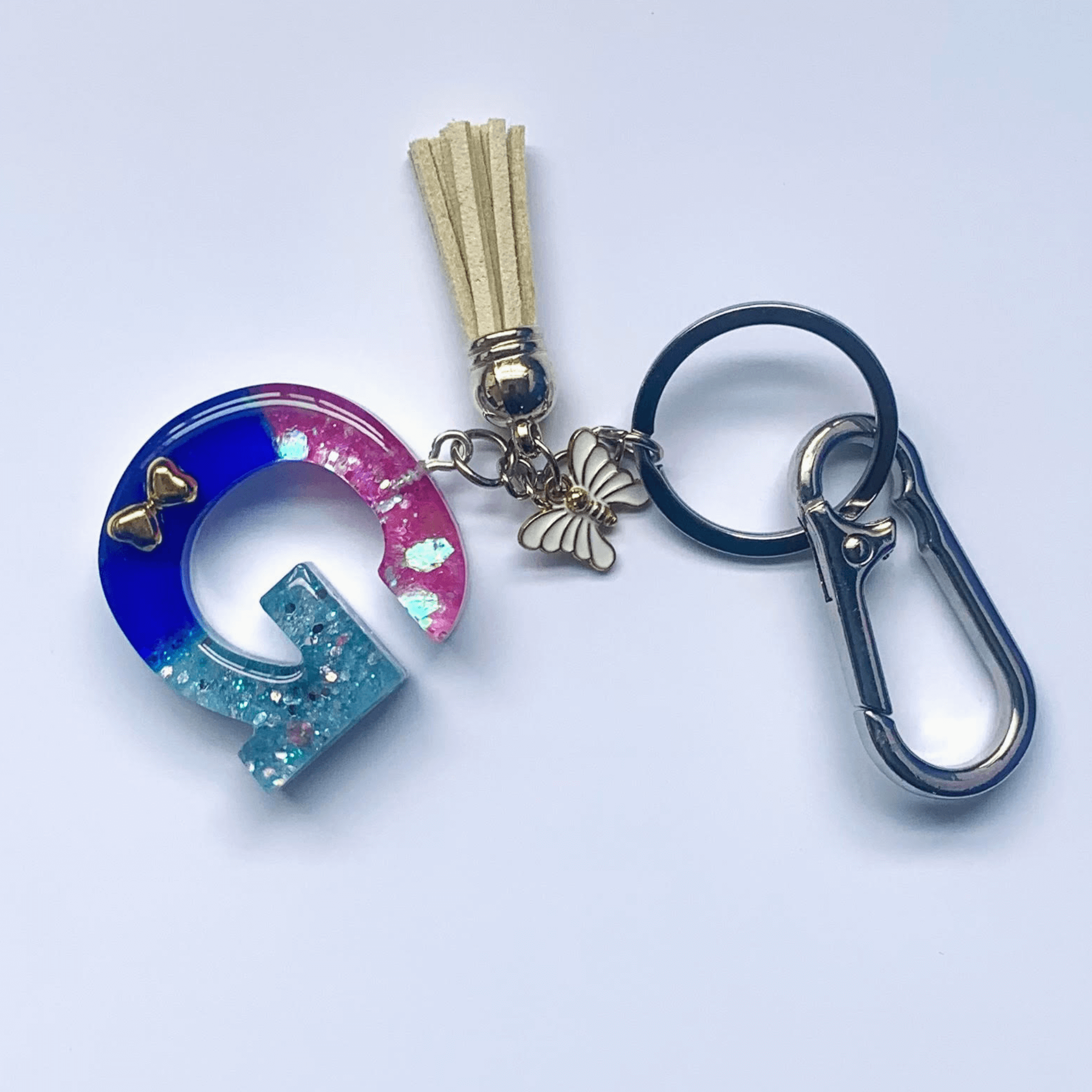 Letter G Keychain with Carabiner – Glitter & Tassel Charm featuring a blue and pink design with tassel and butterfly embellishment.