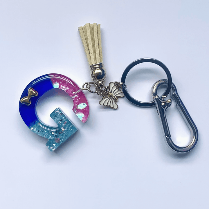 Letter G Keychain with Carabiner – Glitter & Tassel Charm featuring a blue and pink design with tassel and butterfly embellishment.