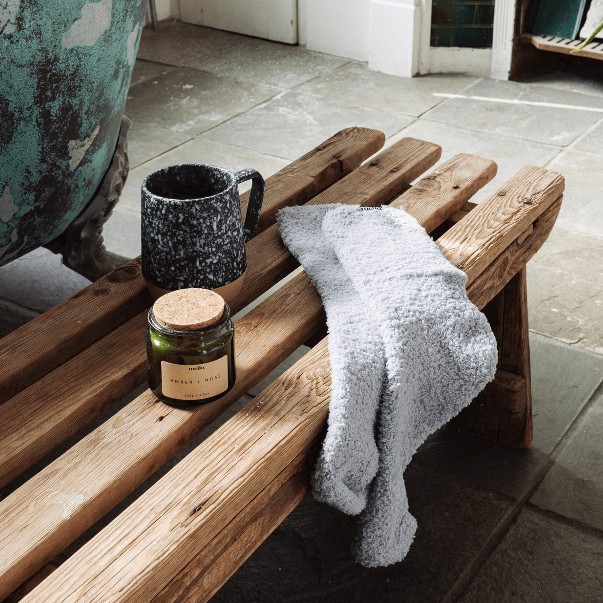Mello Max Relax displayed on a wooden bench with a mug, candle, and towel for a cozy ambiance.