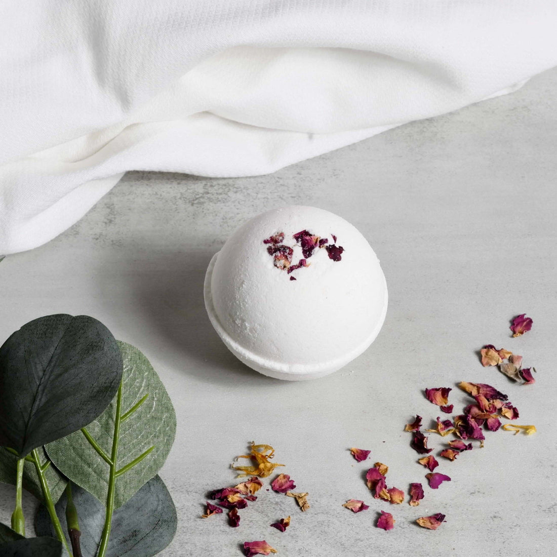 Natural bath bomb with rose petals on a gray surface, part of the Rosy Glow for Mom Gift Box.