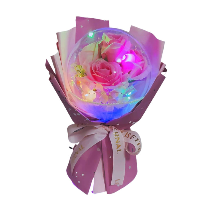 Pink rose bouquet in acrylic dome with lights, gift-wrapped in purple and pink paper.