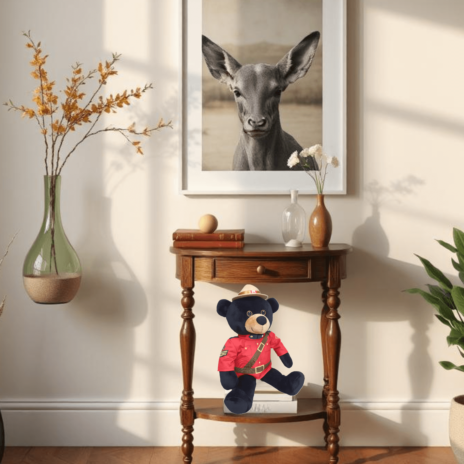 RCMP Sergeant Black Bear plush toy in red serge uniform on a wooden table beside a deer picture.