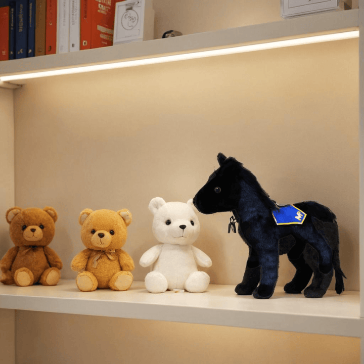 RCMP Standing Plush Horse displayed on a shelf beside teddy bears, showing its black plush body and blue RCMP saddle blanket.