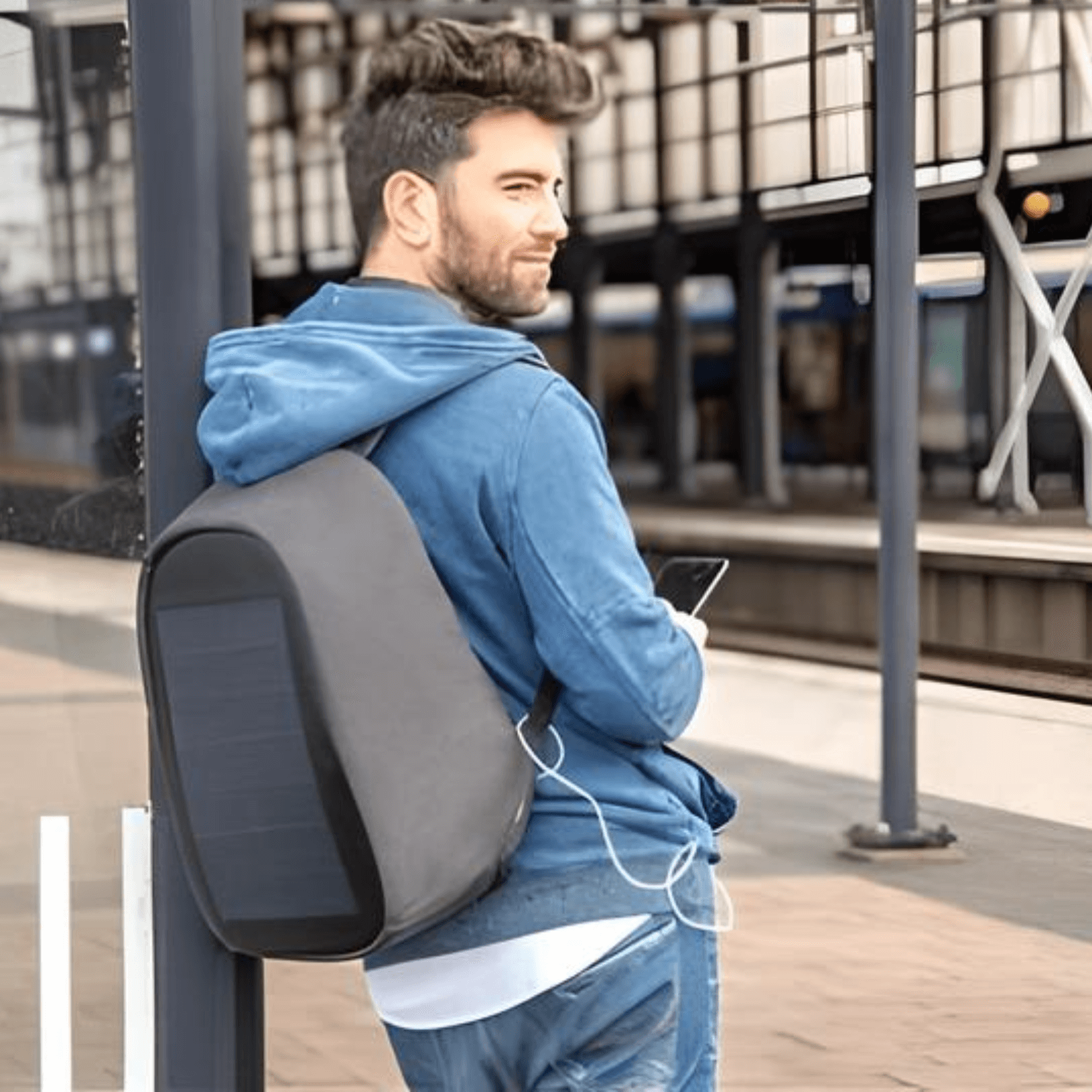Man at train station wearing XD Design Bobby Tech Anti-Theft Backpack with solar panel for charging devices.